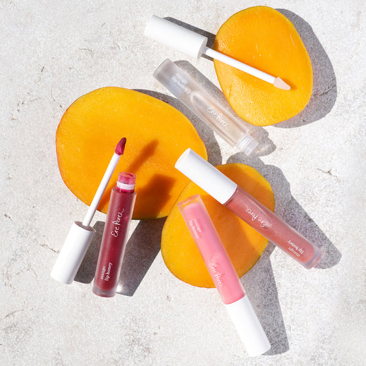 vista aerea de envases abiertos de lipgloss con mango ere perez en todos sus tonos con rebanadas de mango