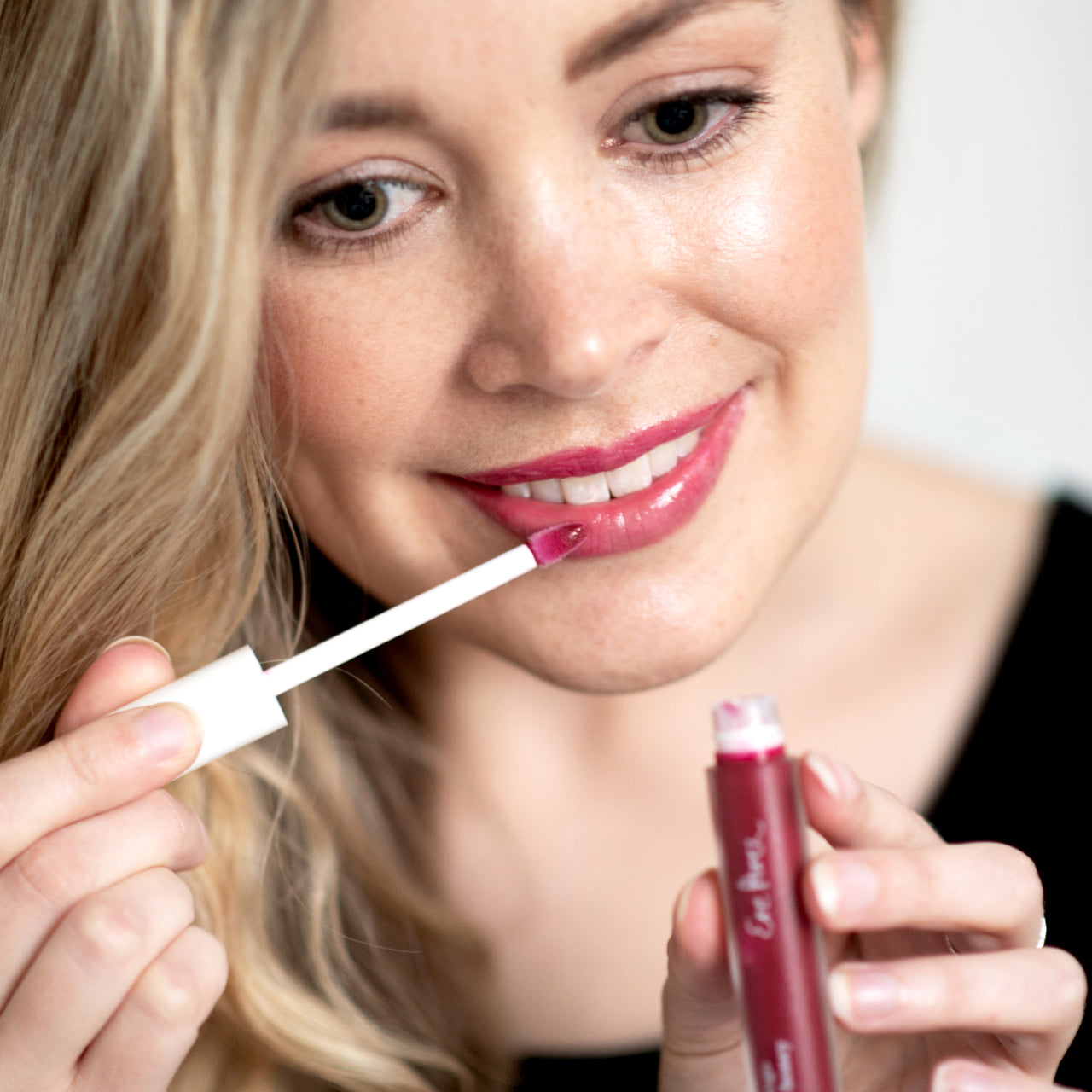mujer sonriendo mostrando en sus labios el tono crush del lipgloss con mango ere perez y en sus manos el envase