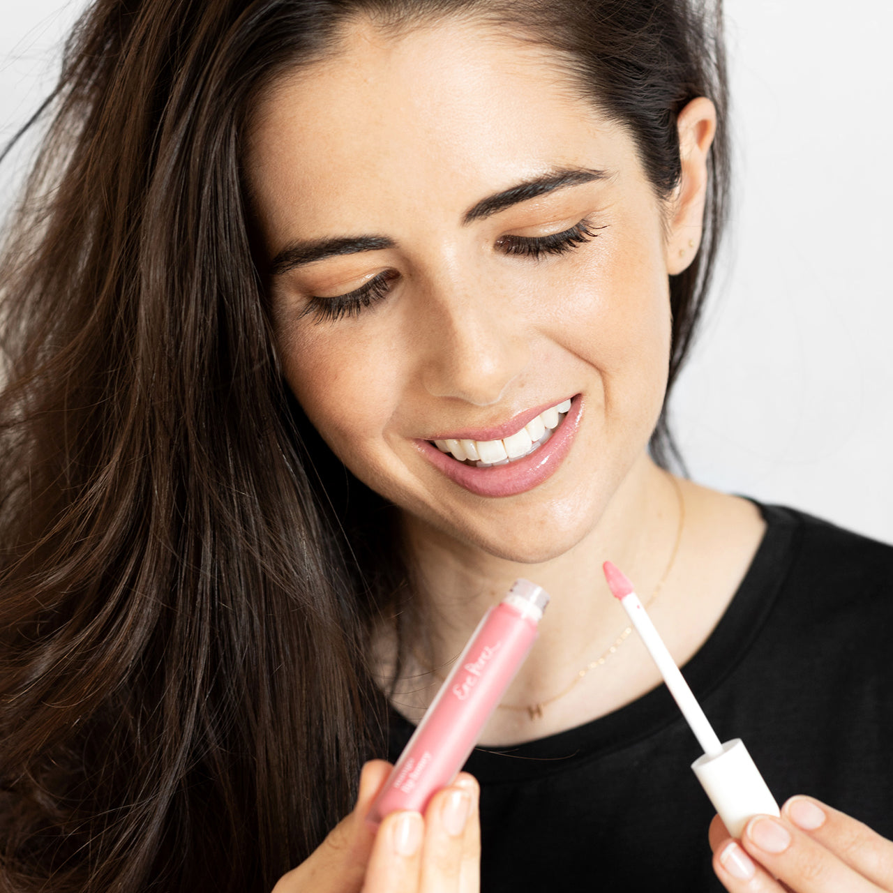 mujer sonriendo mostrando en sus manos el tono pop del lipgloss con mango ere perez y sus labios brillantes