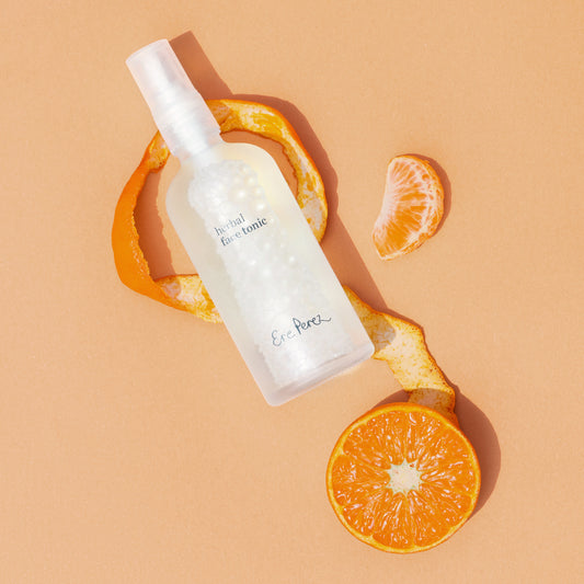 vista aerea del tonico facial herbal sobre cascara de mandarina con gajos a lado en fondo color durazno ere perez disponible en blumma