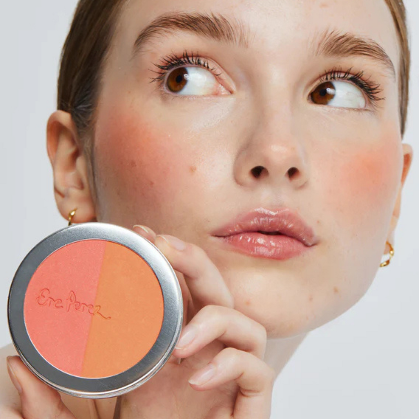 mujer sonriendo con tono bondi en sus mejillas de blush y bronceador ere perez sosteniendo envase disponible en blumma