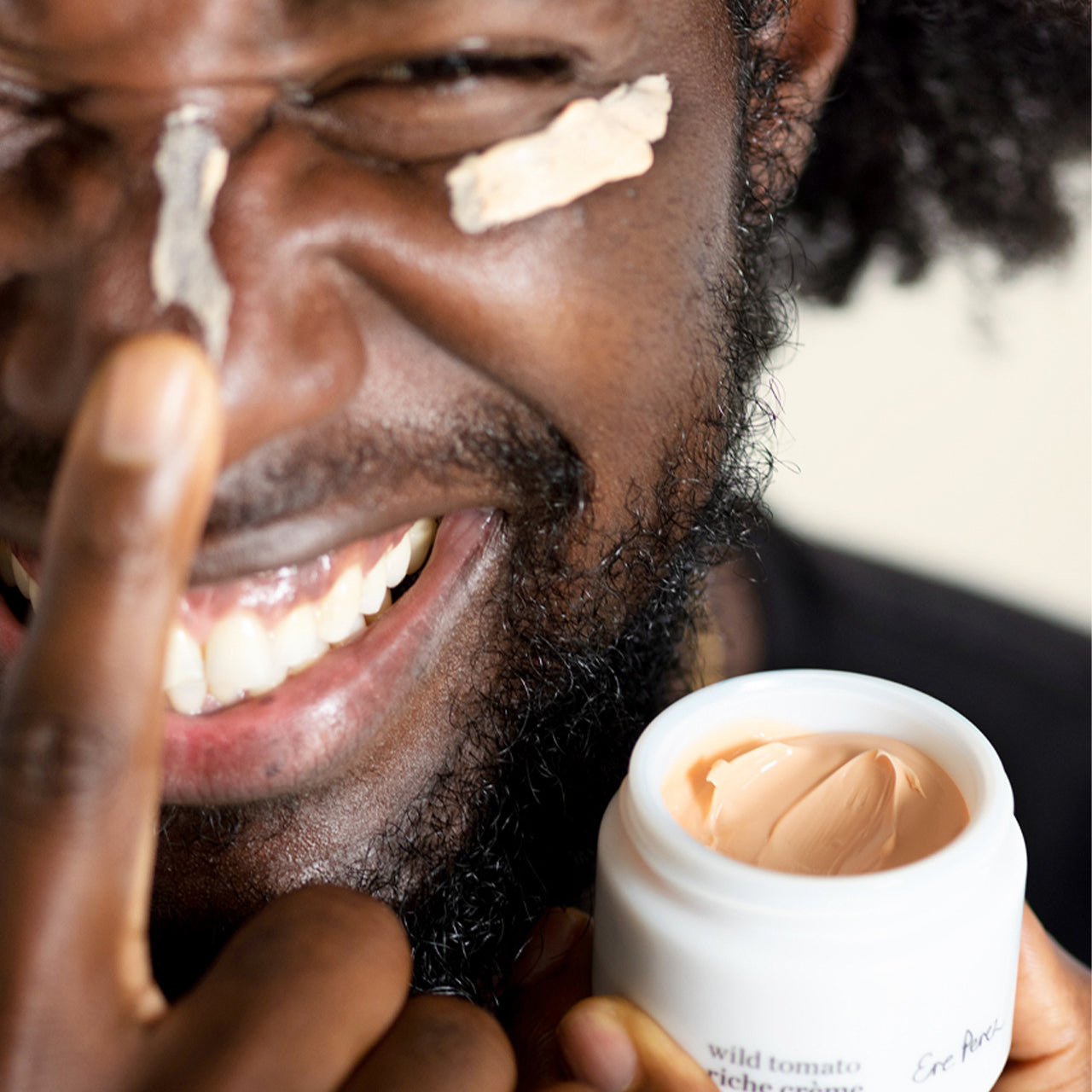 Hombre sonriendo aplicando hidratante facial Ere Perez con jitomate en mejilla, disponible en BLUMMA