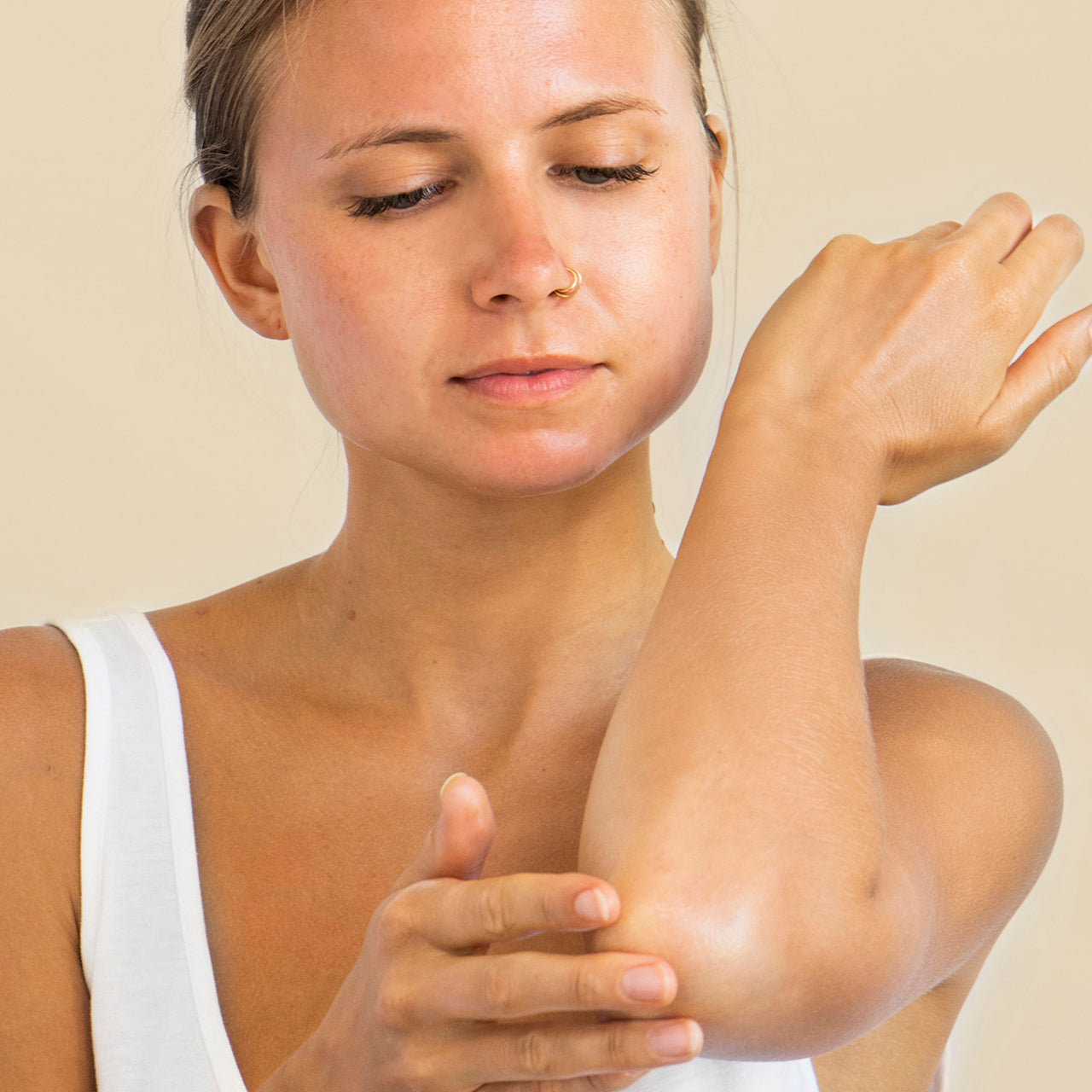 mujer aplicando jalea sos con papaya Ere Perez en los codos resecos en fondo minimalista disponible en BLUMMA