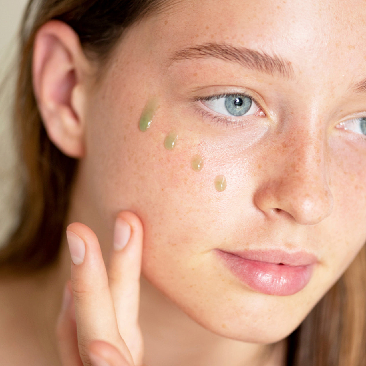 retrato de modelo de tez clara y ojos azules con cuatro gotas del suero verde hidratante en su mejilla ere perez disponible en blumma