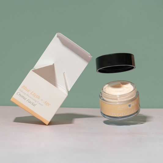 vista frontal de envase de vidrio transparente junto con empaque de la crema facial blue light + age de avoroots