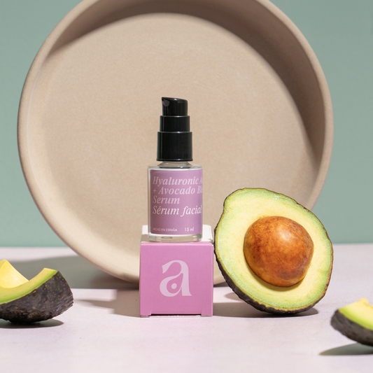 vista frontal de envase de vidrio transparente junto con empaque del suero de acido hialuronico con aguacate de avoroots