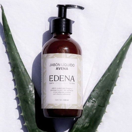 vista frontal de envase de vidrio color ambar del jabon liquido de avena sobre plantas de sabila edena