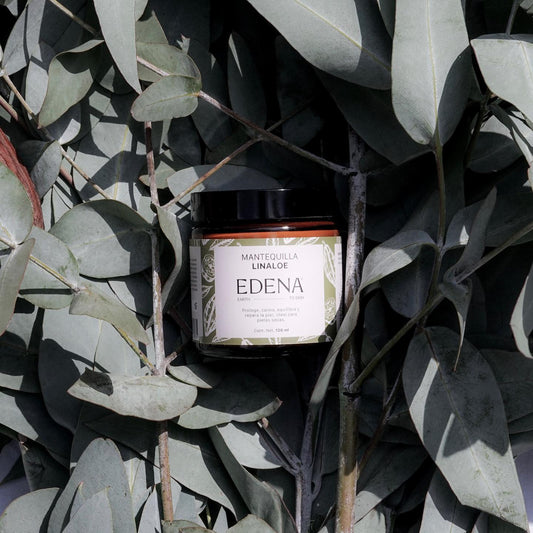 vista frontal de envase de vidrio color ambar de la mantequilla de linaloe de edena en fondo con plantas edena