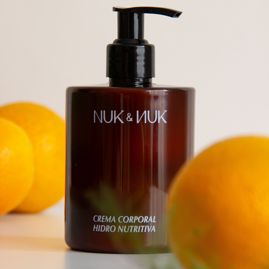 vista frontal de envase de plastico color ambar de la crema corporal hidronutritiva de nuk y nuk en fondo blanco con naranjas