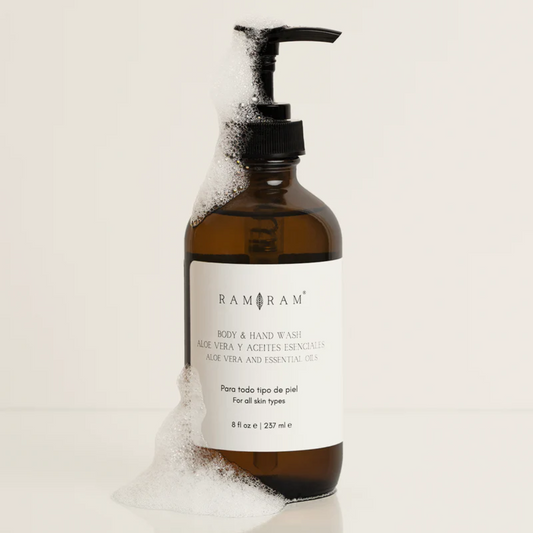 vista frontal de envase de vidrio color ambar del jbon liquido corporal de aloe vera con aceites esenciales de ram ram con espuma en fondo blanco