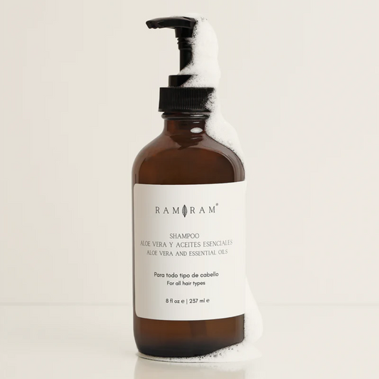 vista frontal de envase de vidrio color ambar del shampoo de aloe vera con aceites esenciales de ram ram con espuma en fondo blanco