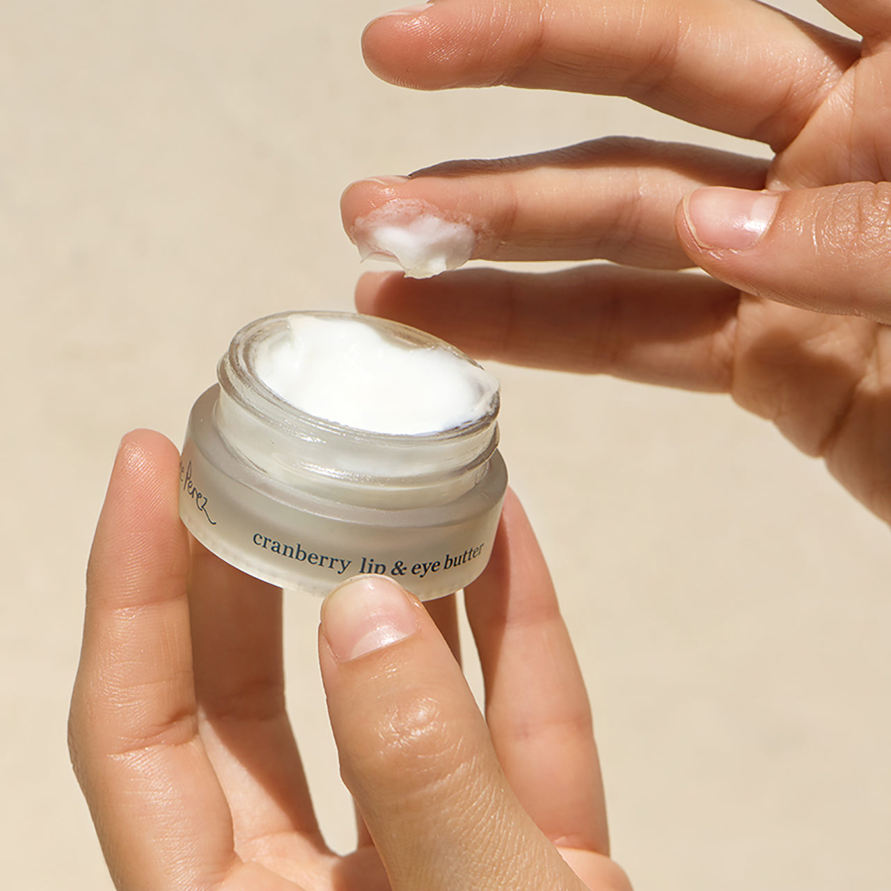 Mano deteniendo frasco de crema con arandano para ojos y labios Ere Perez probando textura disponible en BLUMMA