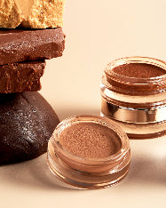 balsamo bronceador de cacao en sus dos tonos junto a barras de manteca de cacao fondo minimalista