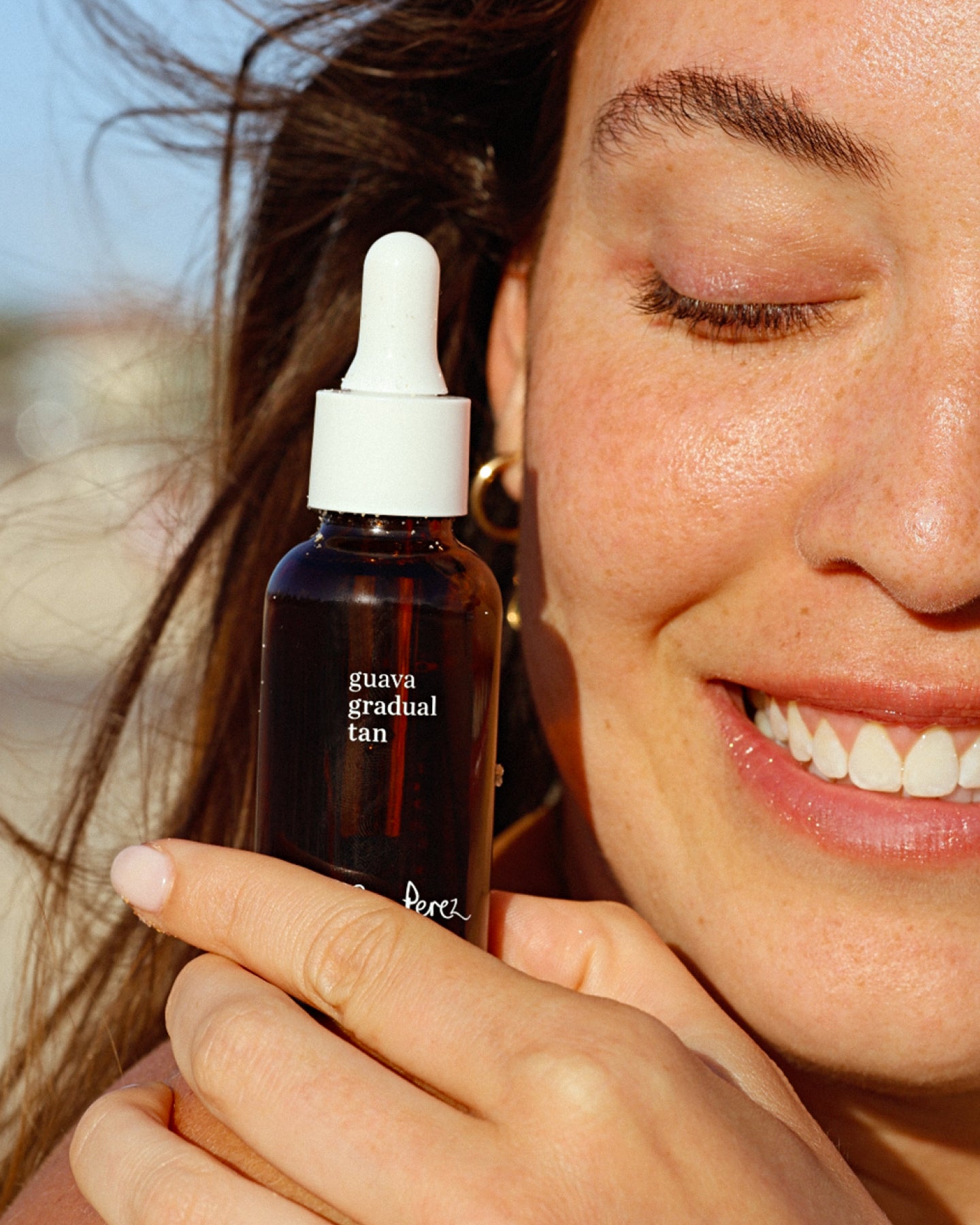 bronceador gradual de guayaba sujetado por mujer sonriendo disponible en BLUMMA