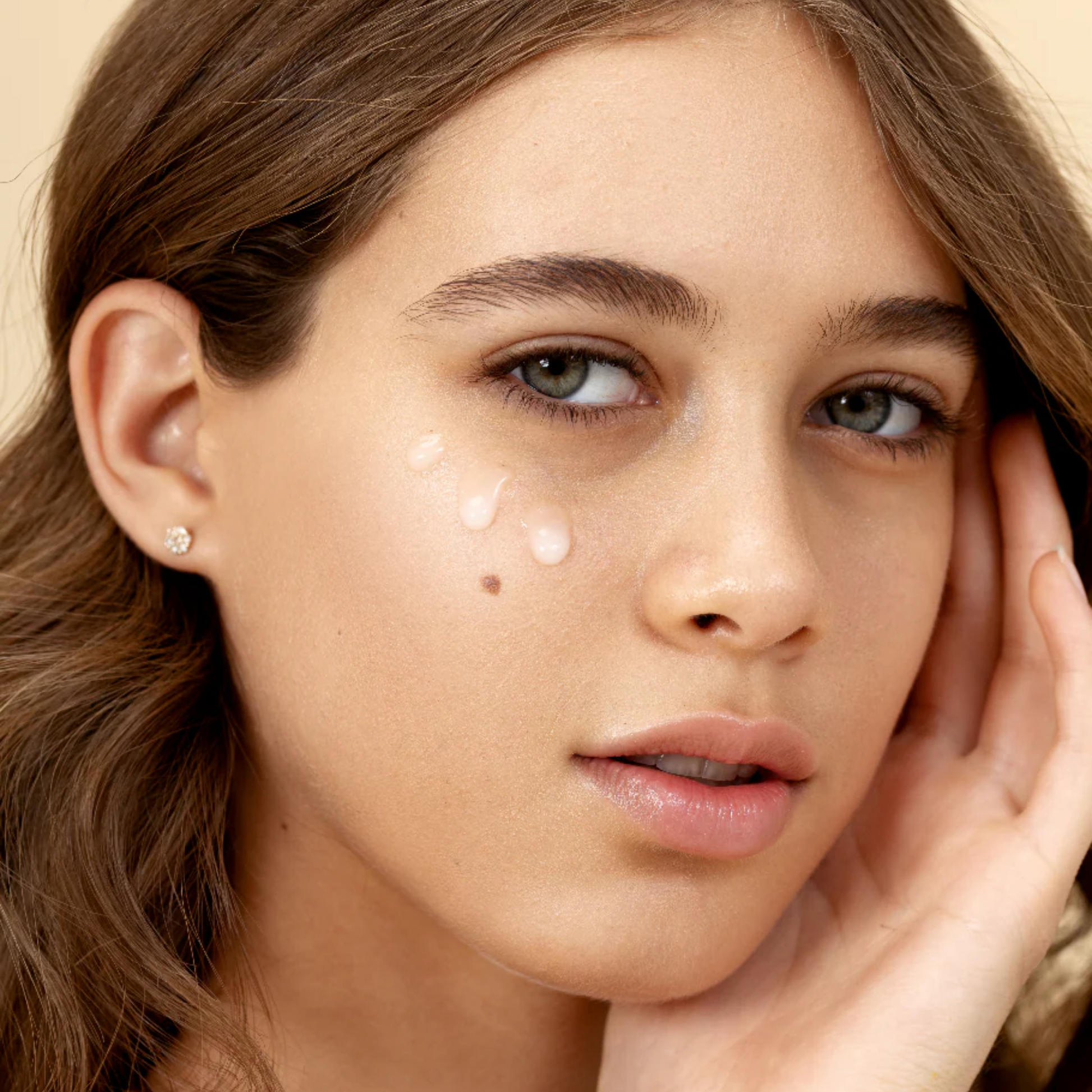 retrato de modelo con tres gotas de suero facial con acido hialuronico y aguacate en las mejillas