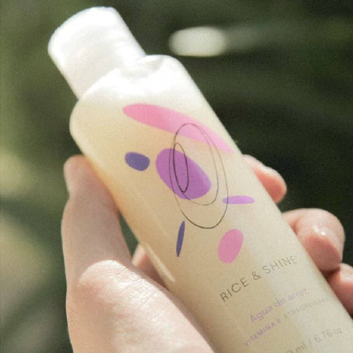 botella de plastico transparente siendo sostenida en una mano y en fondo plantas rice and shine disponible en blumma